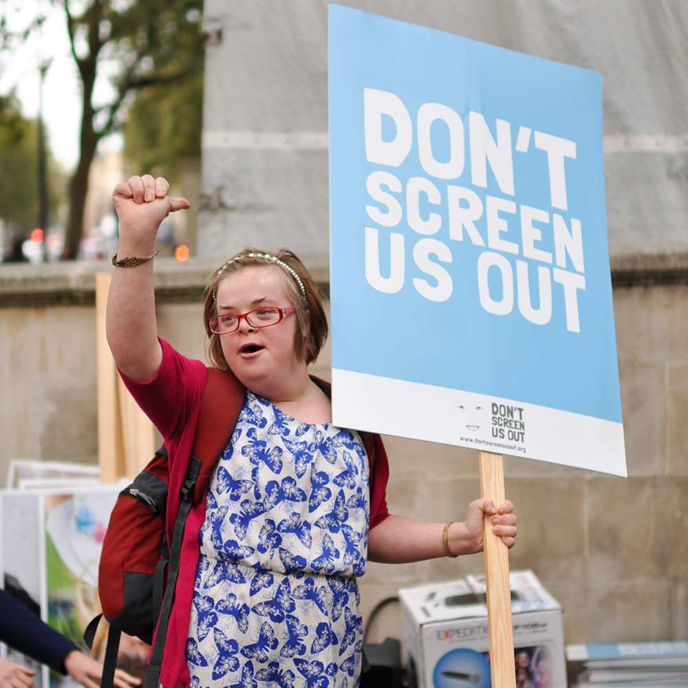 Eine Person hält ein Protestschild mit der Aufschrift "Don't Screen Us Out"