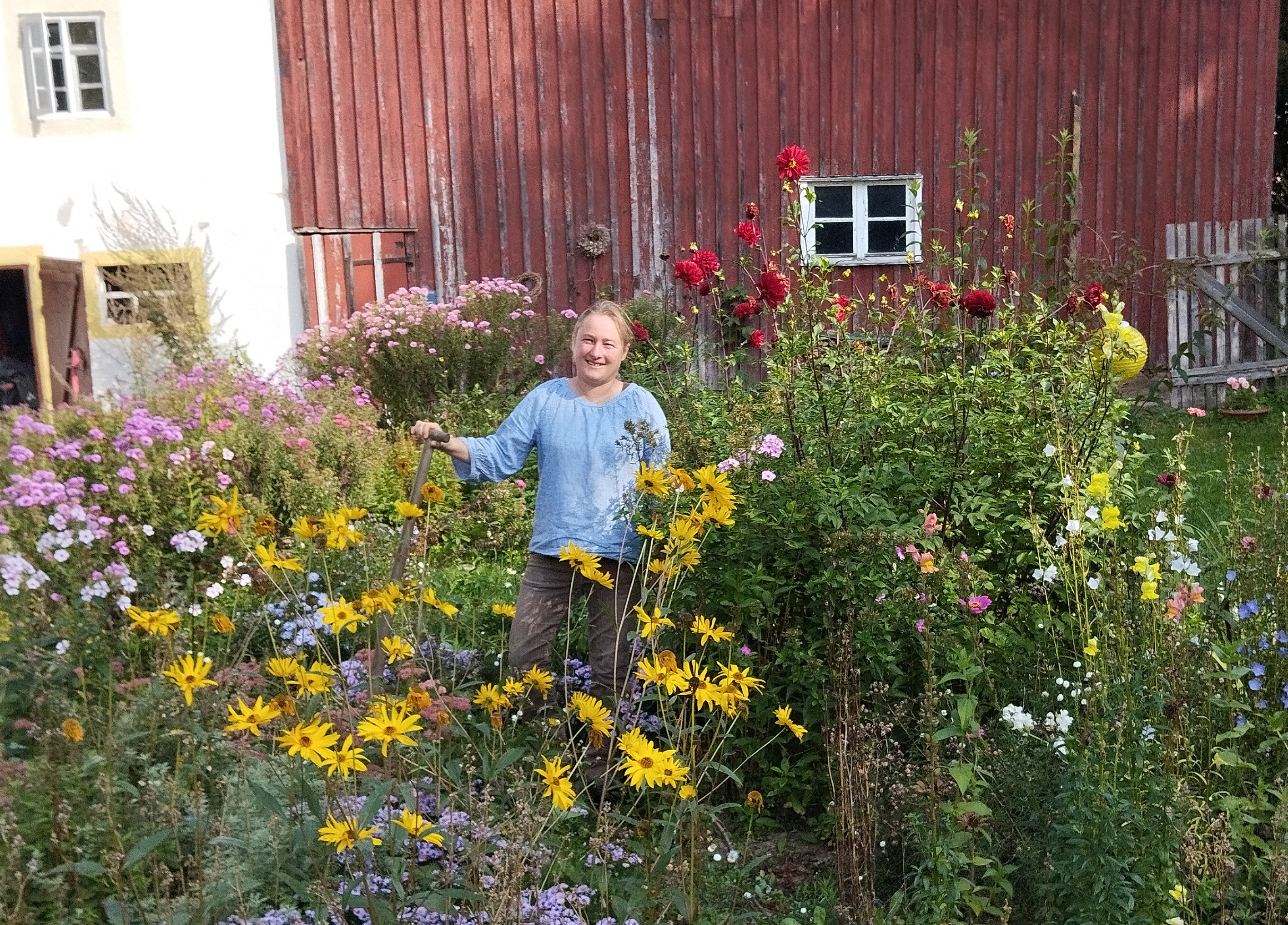 Dr. Anne-Christine Schmidt, blonde Haare mit blauer/grauer Kleidung, steht in ihrem Garten zwischen Blumen. 