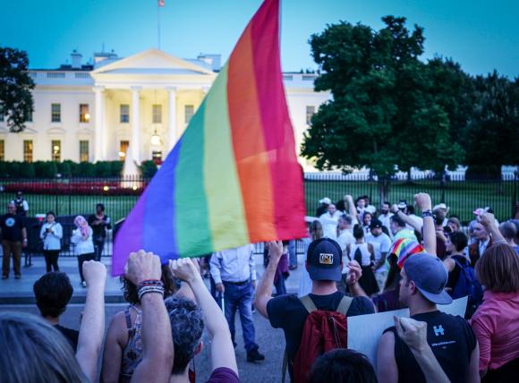 Menschen stehen vor dem Weißen Haus mit einer Regenbogenfahne und gerreckten Fäusten.