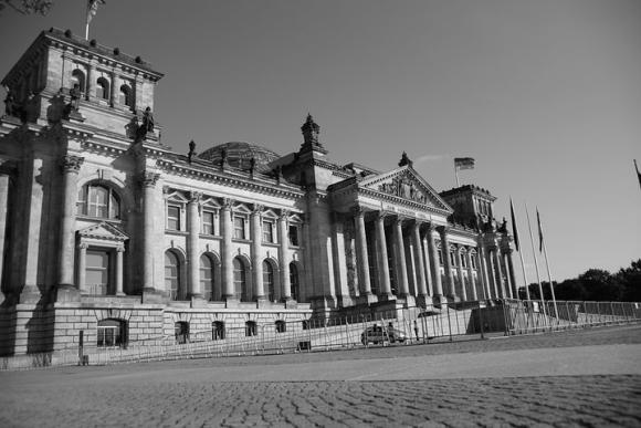 Schwarz-weiß Aufnahme des Reichstagsgebäudes. Es zeigt den Haupteingang, vor den Treppen befinden sich Absperrgitter.