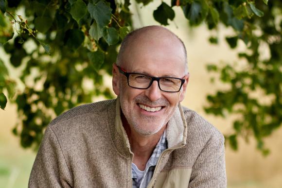 Ein Porträ von Peter Wohlleben. Im Hintergrund sind Äste und Blätter von einem Baum zu erkennen.
